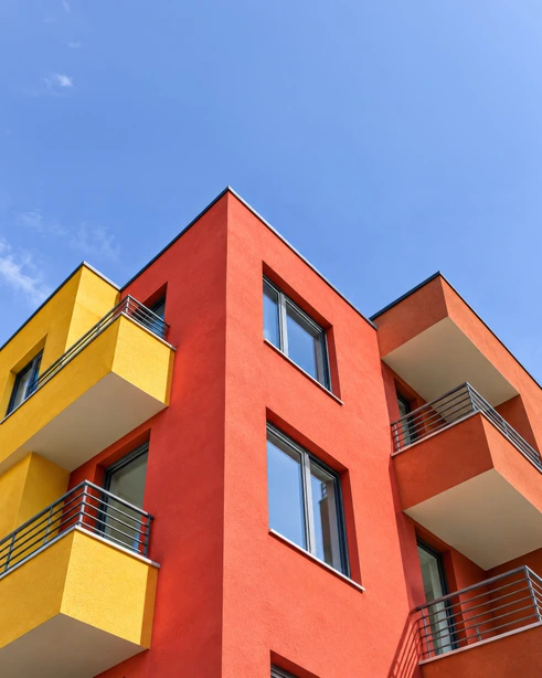 Angolo di un edificio residenziale intonacato in rosso e giallo, con balconi, contro il cielo azzurro