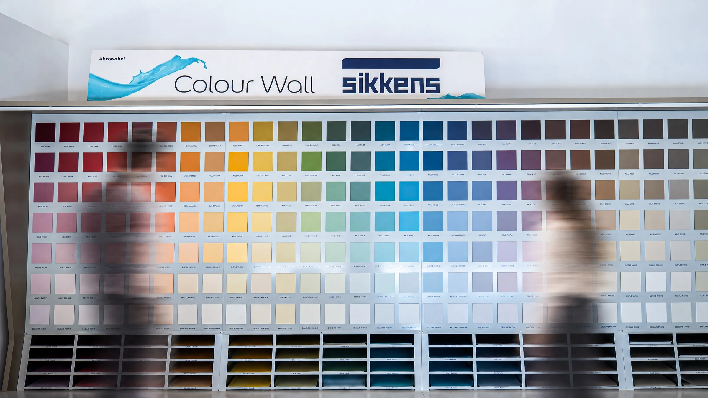 Colour Wall Sikkens con i campioni delle tinte disposti per famiglie e due persone di passaggio sfocate
